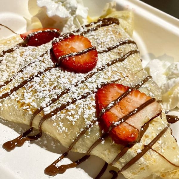 A Brioche de Paris crepe, drizzled with chocolate, powdered sugar, and fresh strawberries.