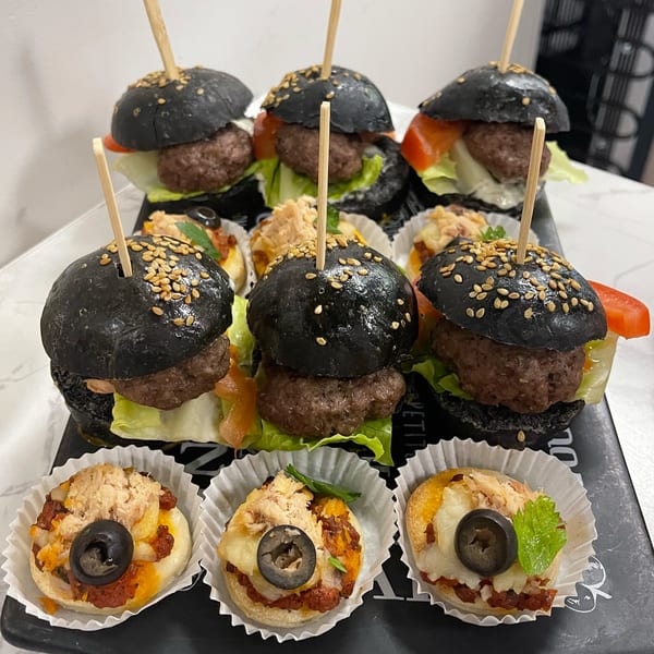 A platter of Brioche de Paris mini black burgers and small savory tarts with olives.