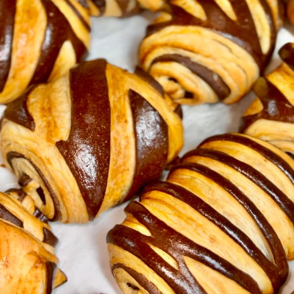 Close-up of several Brioche de Paris chocolate croissants with golden-brown pastry and dark chocolate stripes.