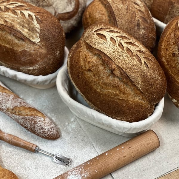 Artisan loaves of bread with decorative scoring, a baguette, and baking tools on a floured surface.